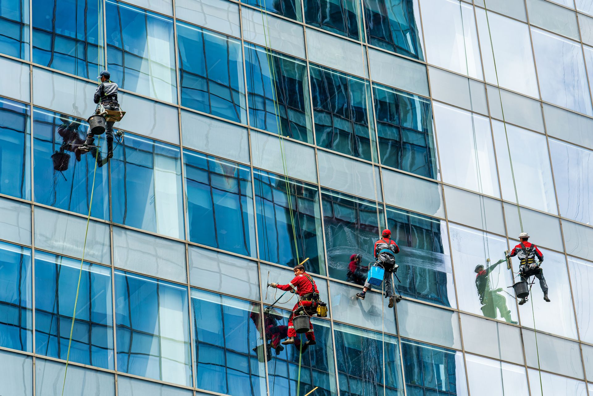 Window washers suspended on ropes cleaning a glass office building facade
