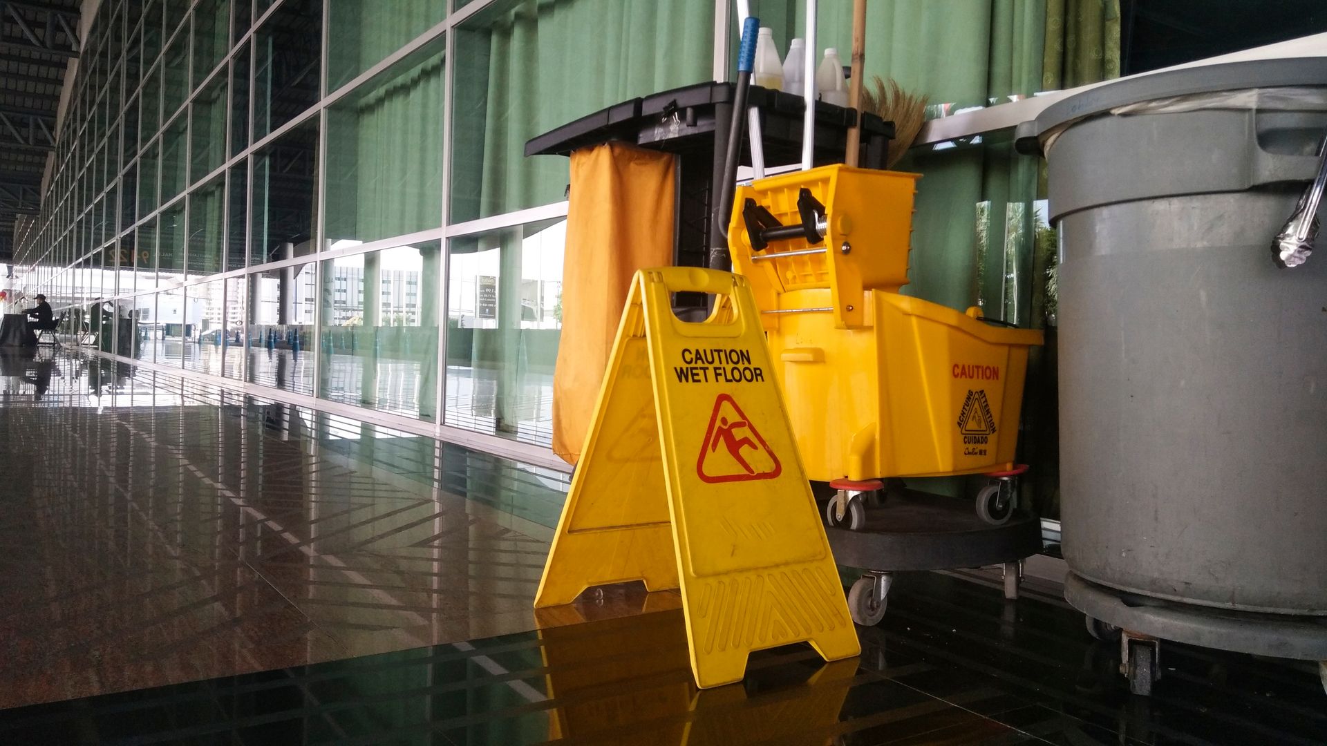 A red mop bucket on wheels with a blue wringer and a long-handled mop resting on a floor.
