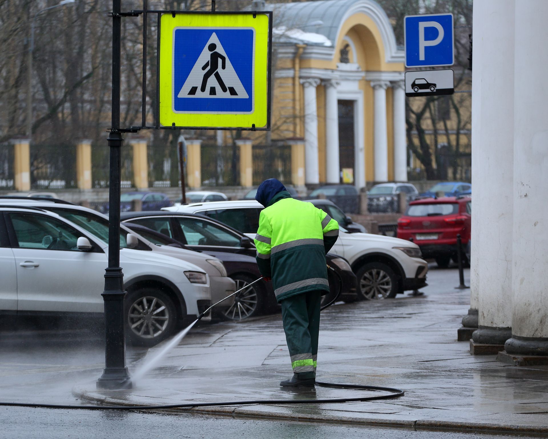 A person in black clothing and boots uses a floor scrubber machine on a wet outdoor concrete surface.