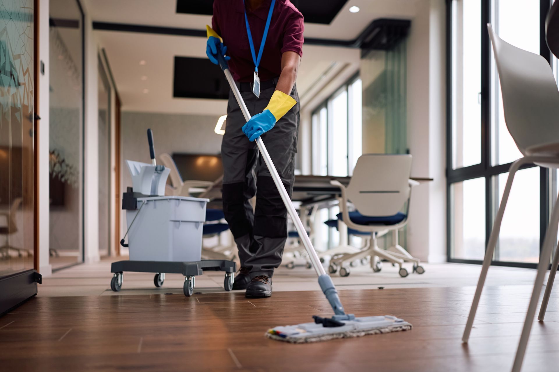 Janitor mopping a hallway floor in a modern office building, with cleaning supplies nearby.