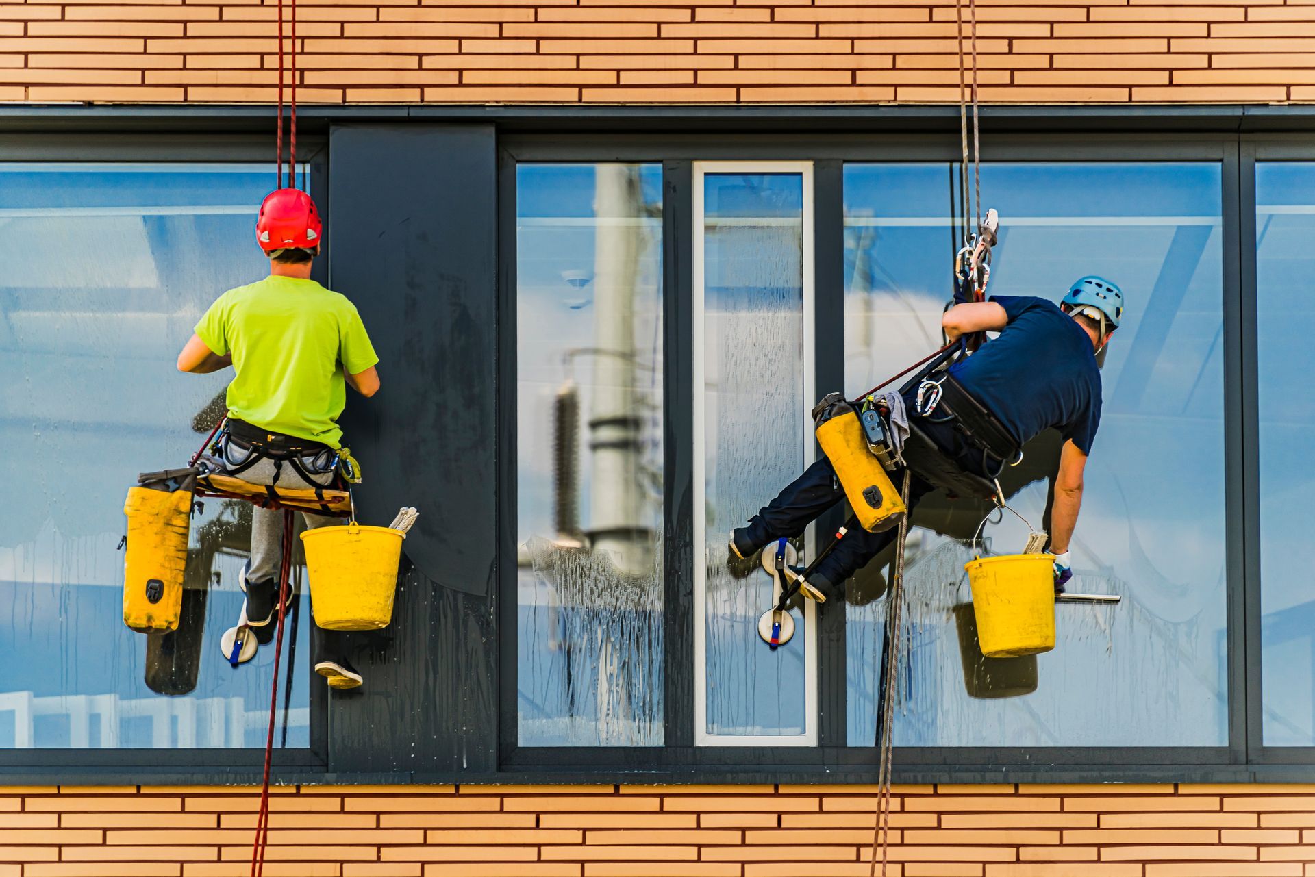 A brush on a pole cleaning a window with water droplets and streaks against a bright blue sky.