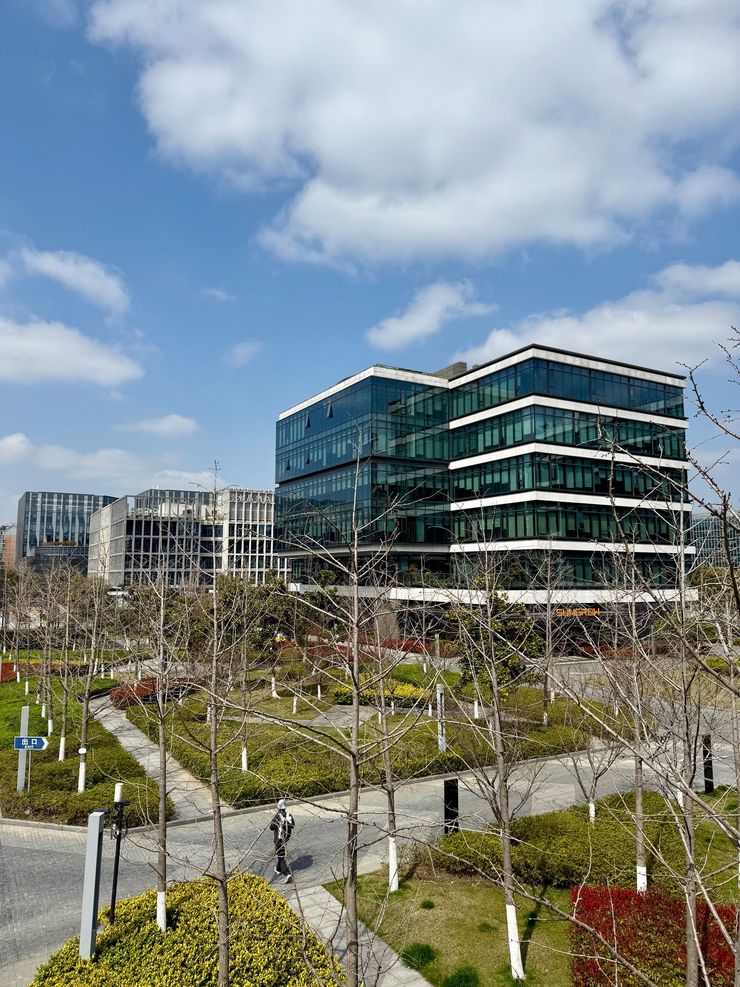 Modern glass office buildings beside a landscaped park with leafless trees under a partly cloudy sky
