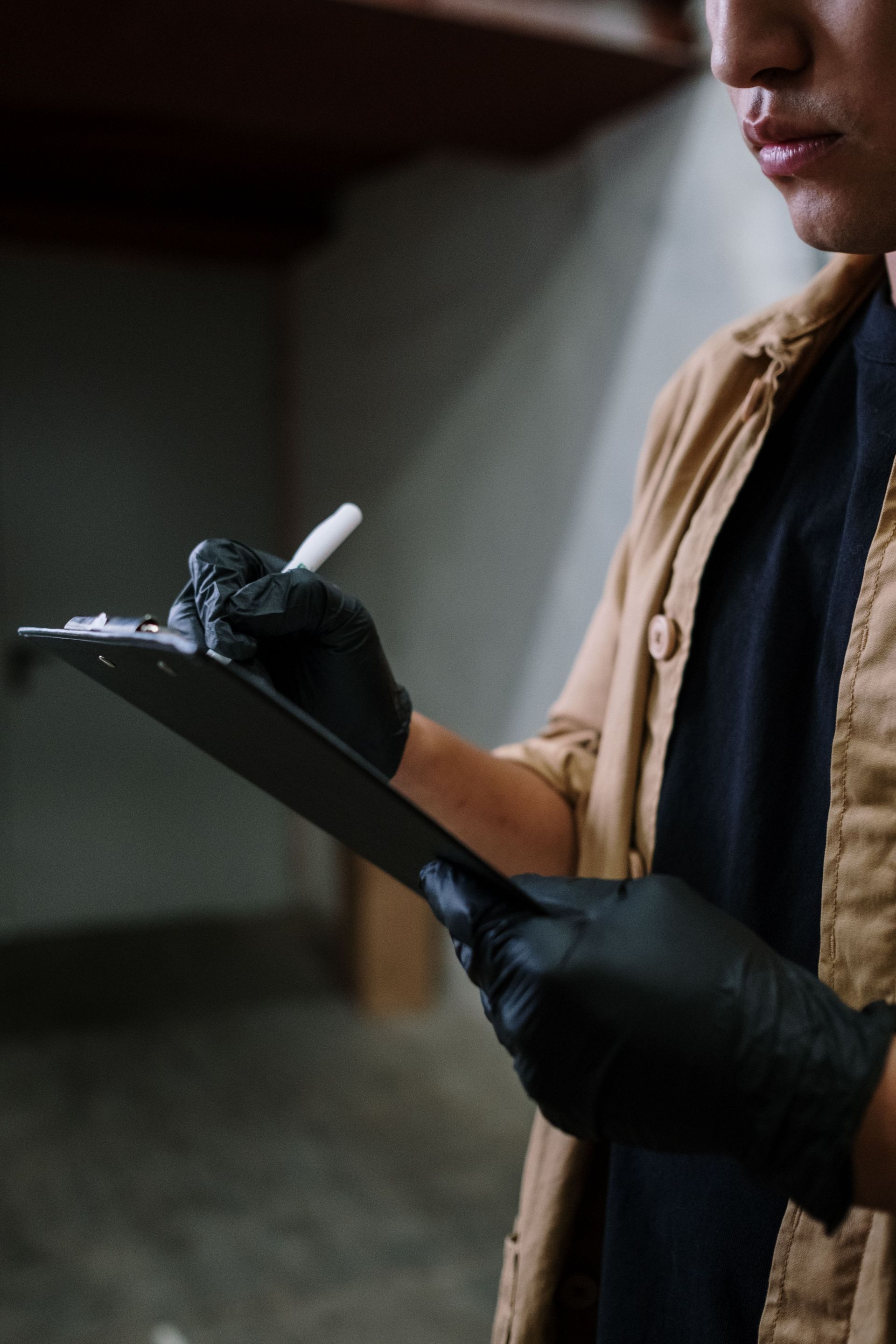 Person in black gloves writing on a clipboard in a dim workshop.