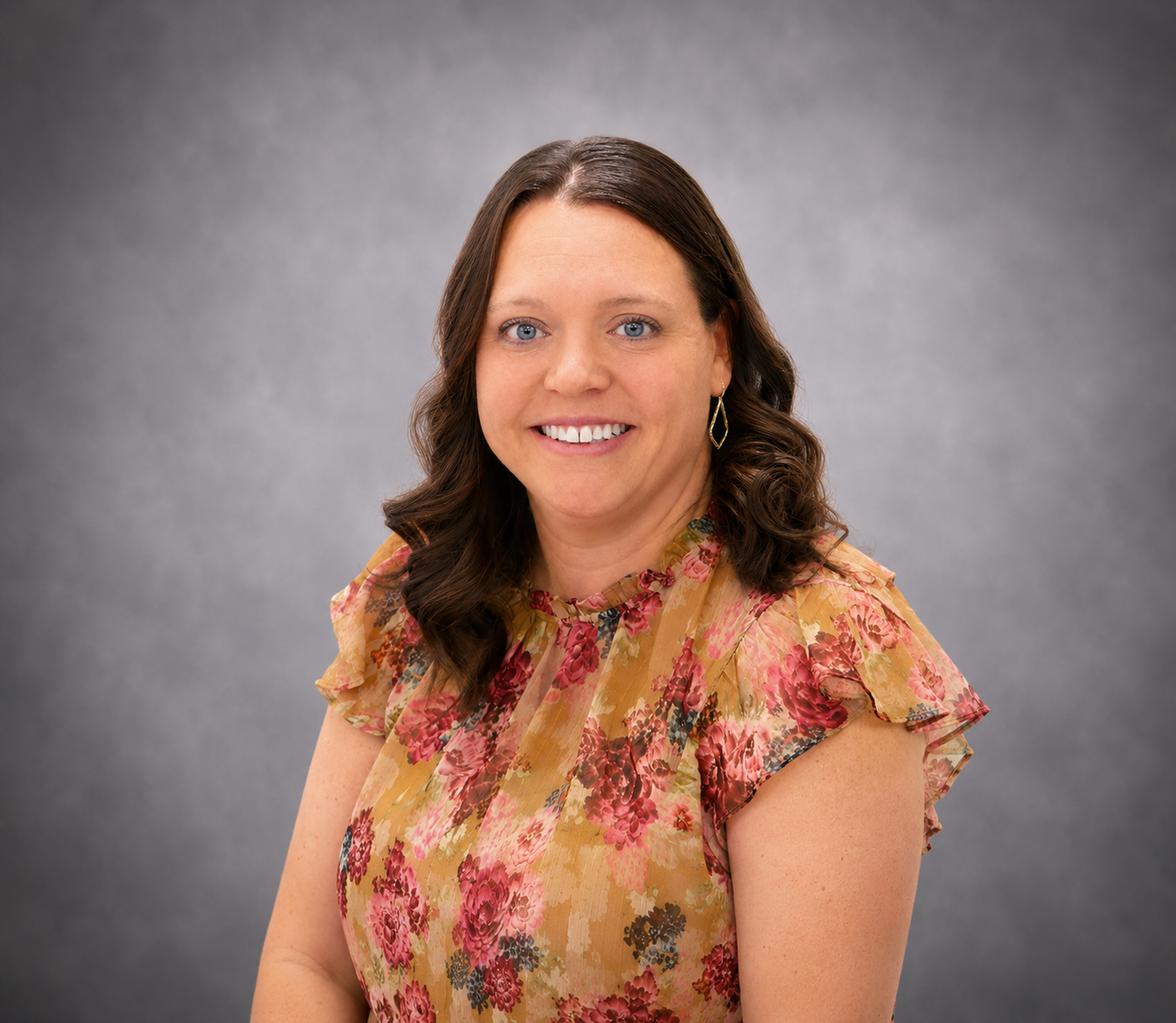 Smiling woman in a floral blouse posing against a gray studio backdrop