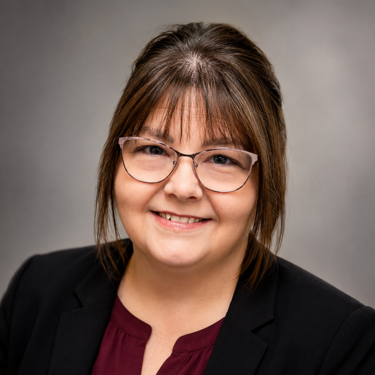 A woman wearing glasses and a purple shirt is smiling for the camera.