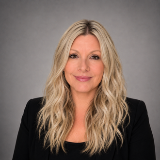 Blonde woman in a black blazer smiling against a gray studio background
