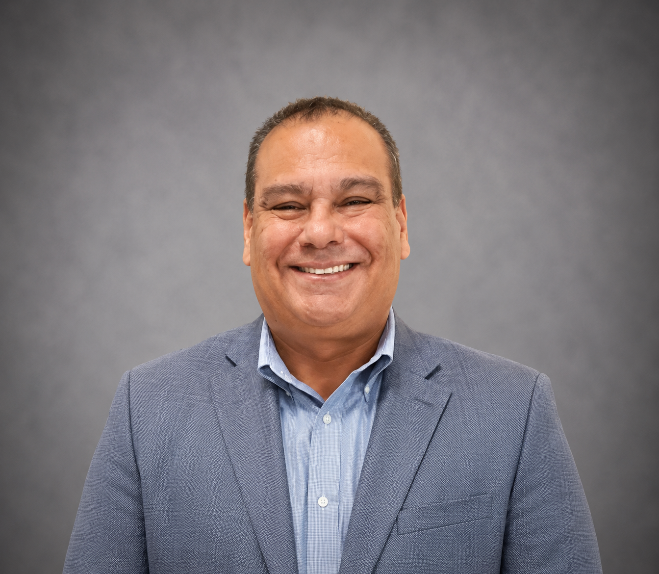 Smiling person in a blue blazer and striped shirt against a gray background