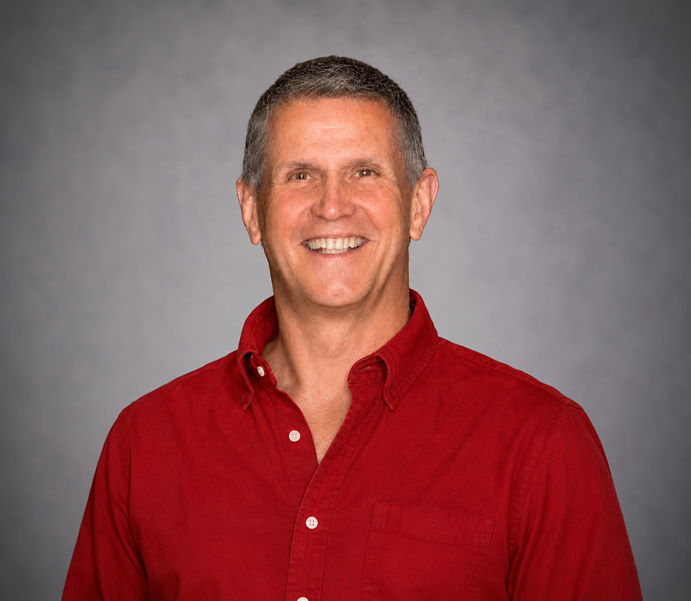 Smiling man in a red button-down shirt against a gray studio background