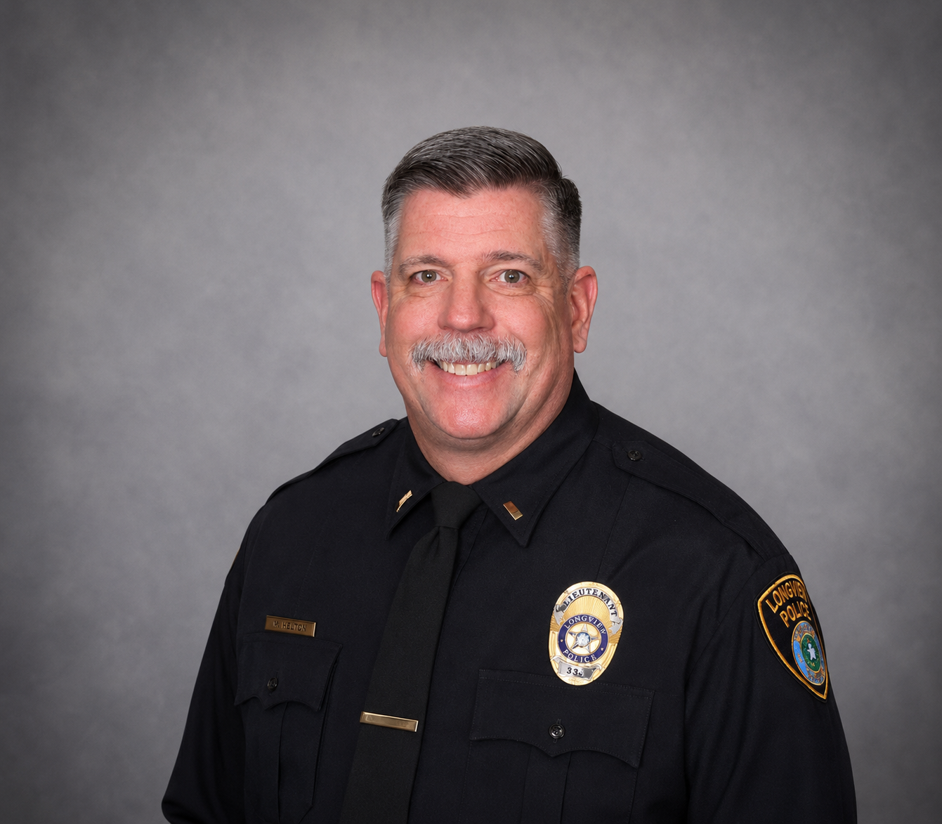 Portrait of a smiling man in a black uniform with sheriff’s badge and patches against a gray backdrop