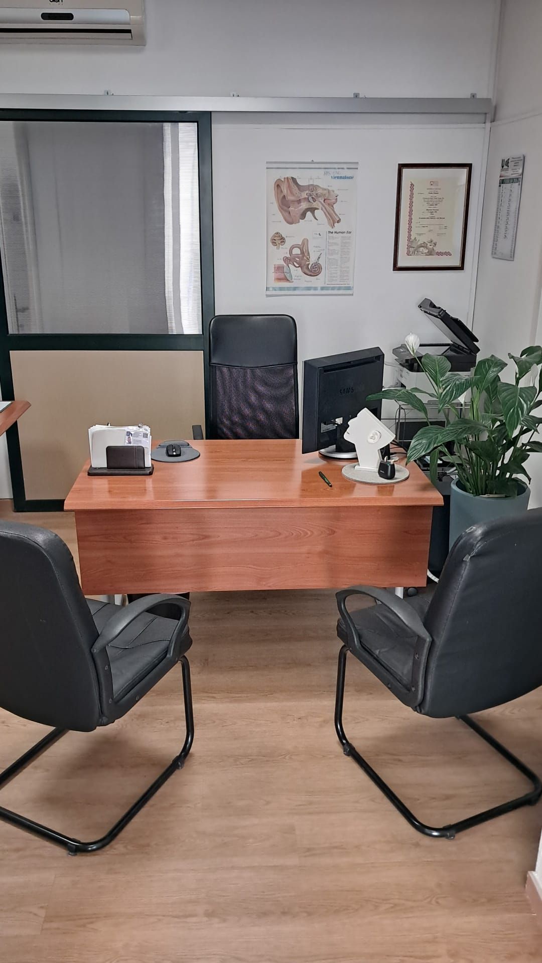 Ufficio con scrivania, sedie, computer e cartelle cliniche alla parete.