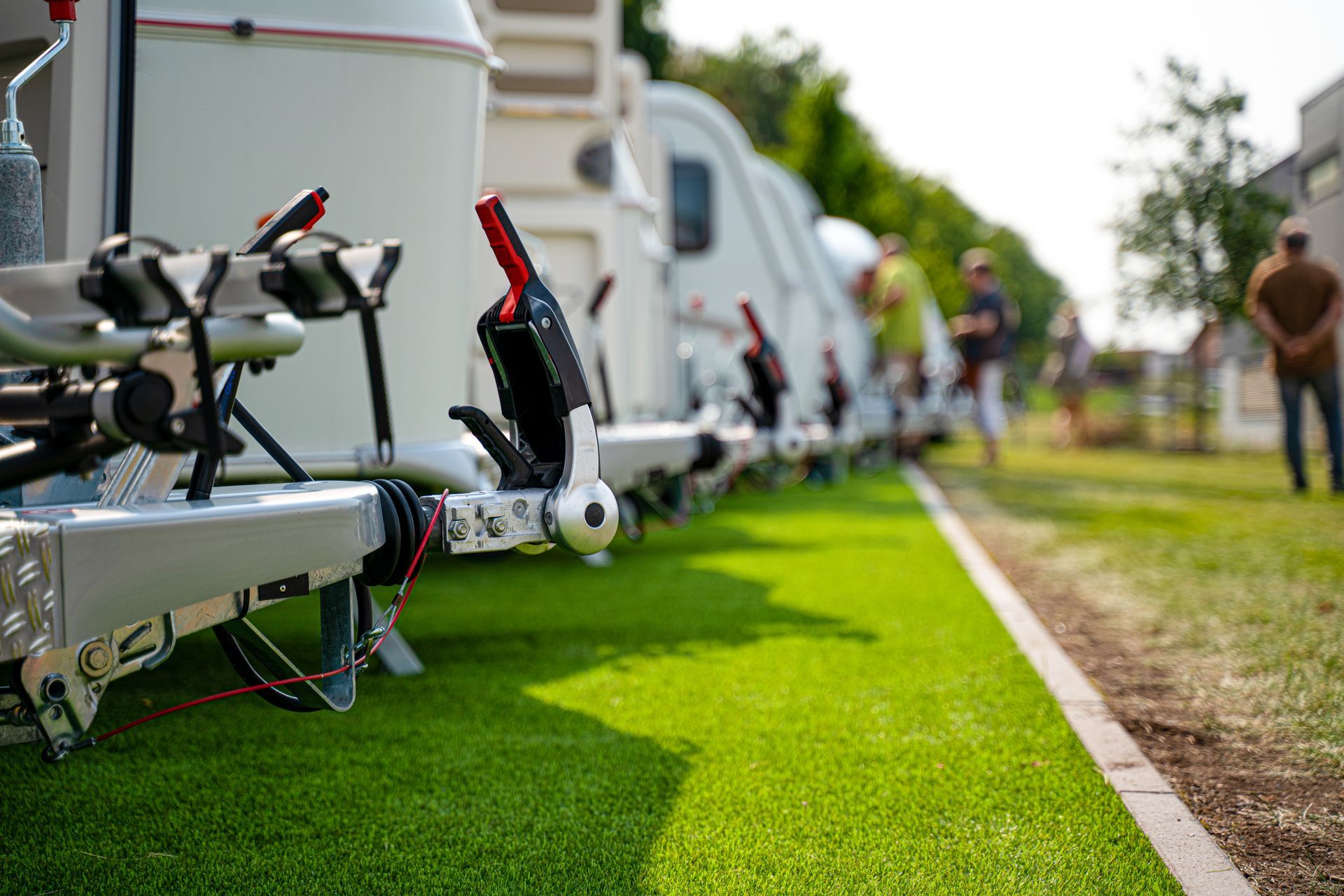 A row of RVs parked on a grassy area with observers, showcasing a recreational vehicle gathering.