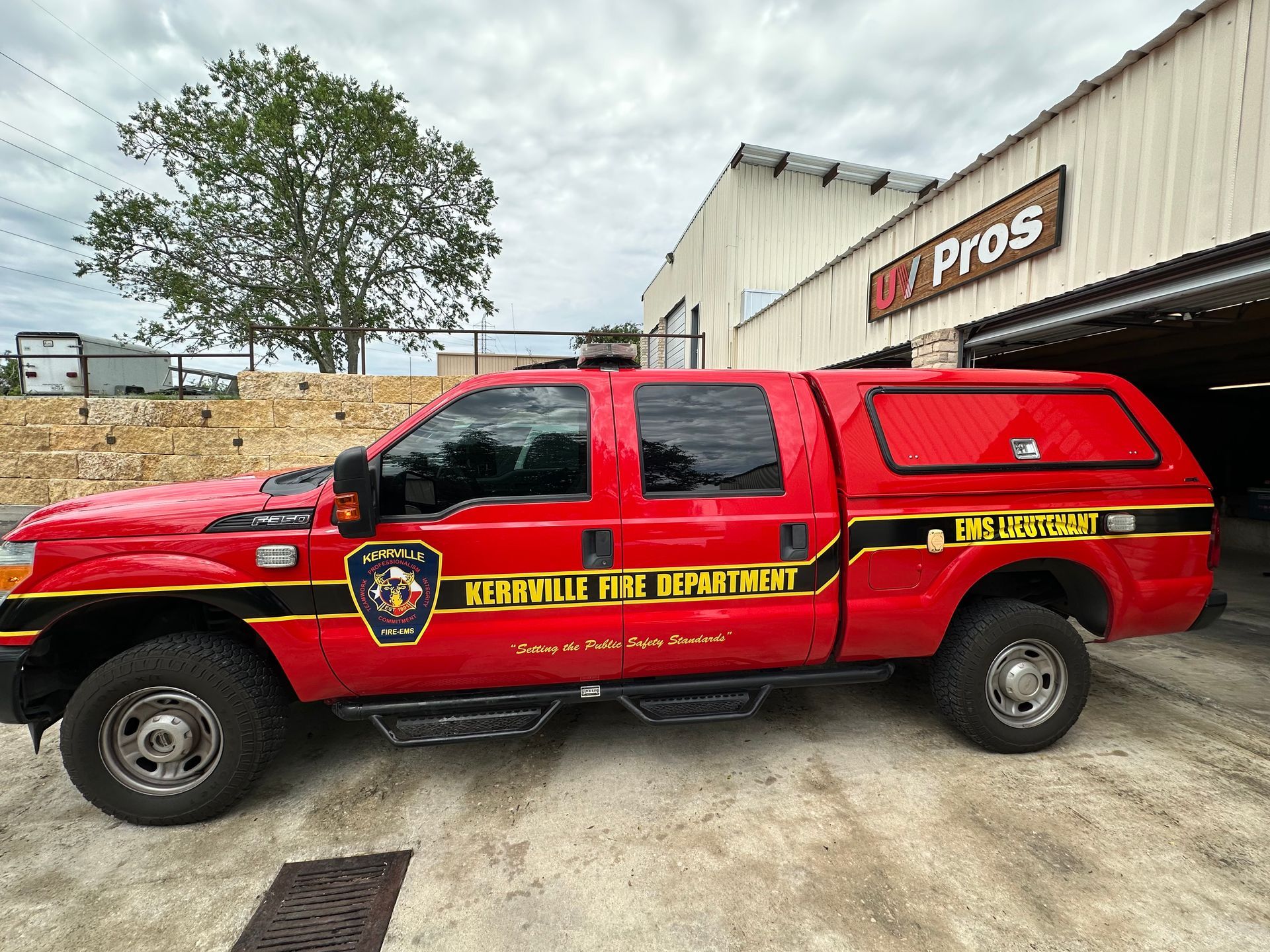 Red Kerrville Fire Department pickup truck parked outside a building with "Pro Pros" signage. The truck has a black stripe and a covered bed.