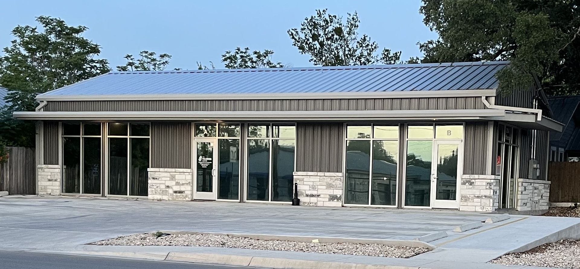 A low, modern building with a metal roof and large windows, set against a blue sky.