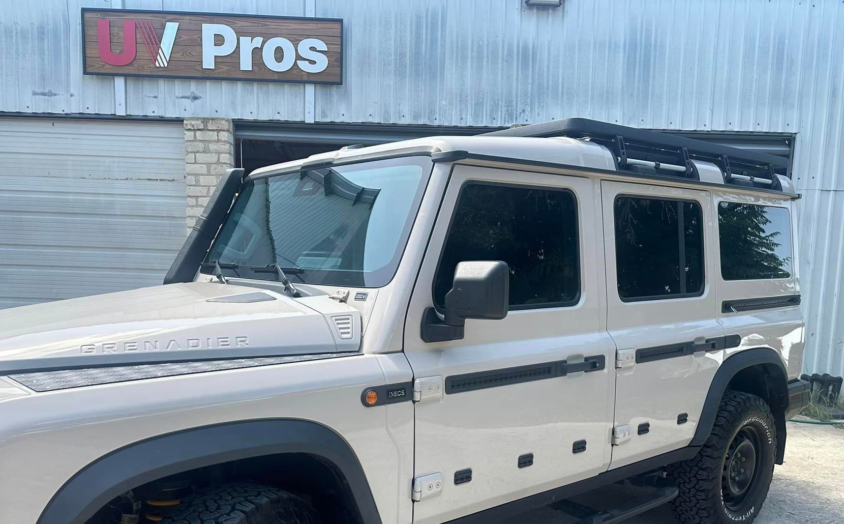 Tan off-road vehicle with a roof rack parked in front of a business,