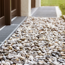 Gravel path in front of a door. Silver grate by the door, leading to the stone pathway.