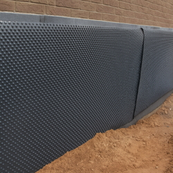 Black dimpled drainage membrane applied to a foundation wall, protecting against moisture.