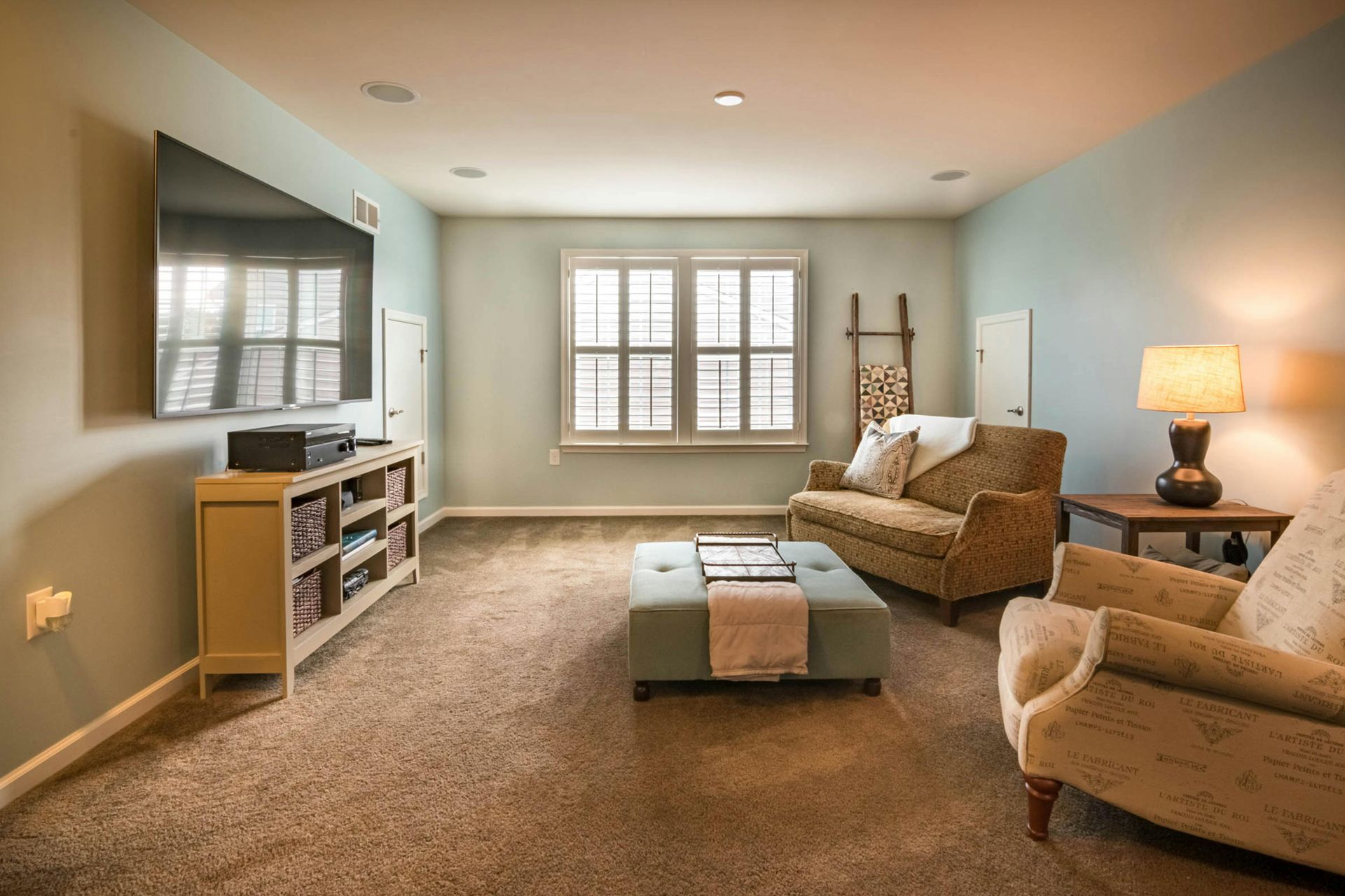 Living room with TV, beige carpet, blue walls, a window, sofa, and chairs.