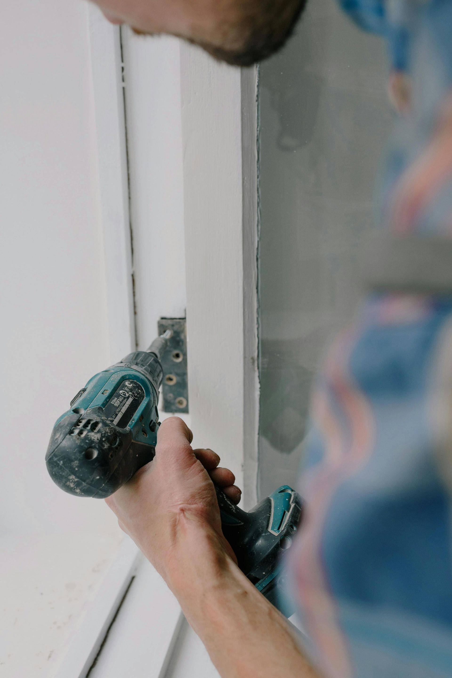 Person using a power drill to attach a hinge to a door frame.