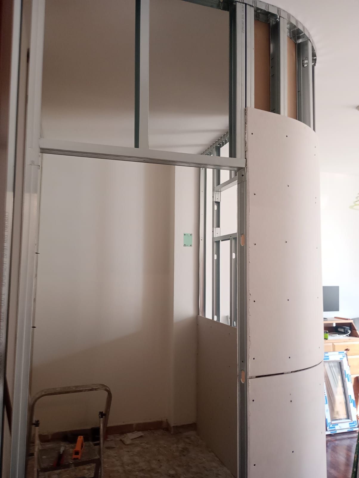 Interno di una stanza parzialmente intelaiata con montanti a parete curvi e una piccola scaletta sul pavimento.