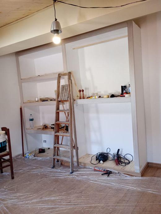 Stanza parzialmente ristrutturata con scala, mensole a vista, lampada a sospensione e attrezzi sul pavimento.