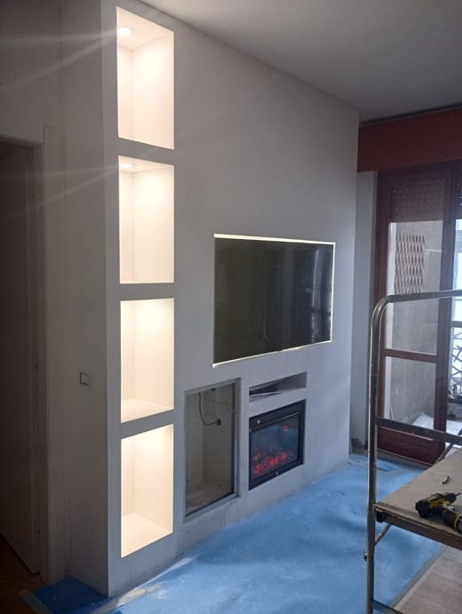 Soggiorno moderno con TV a parete, camino elettrico e ampi pannelli finestrati satinati sulla sinistra.