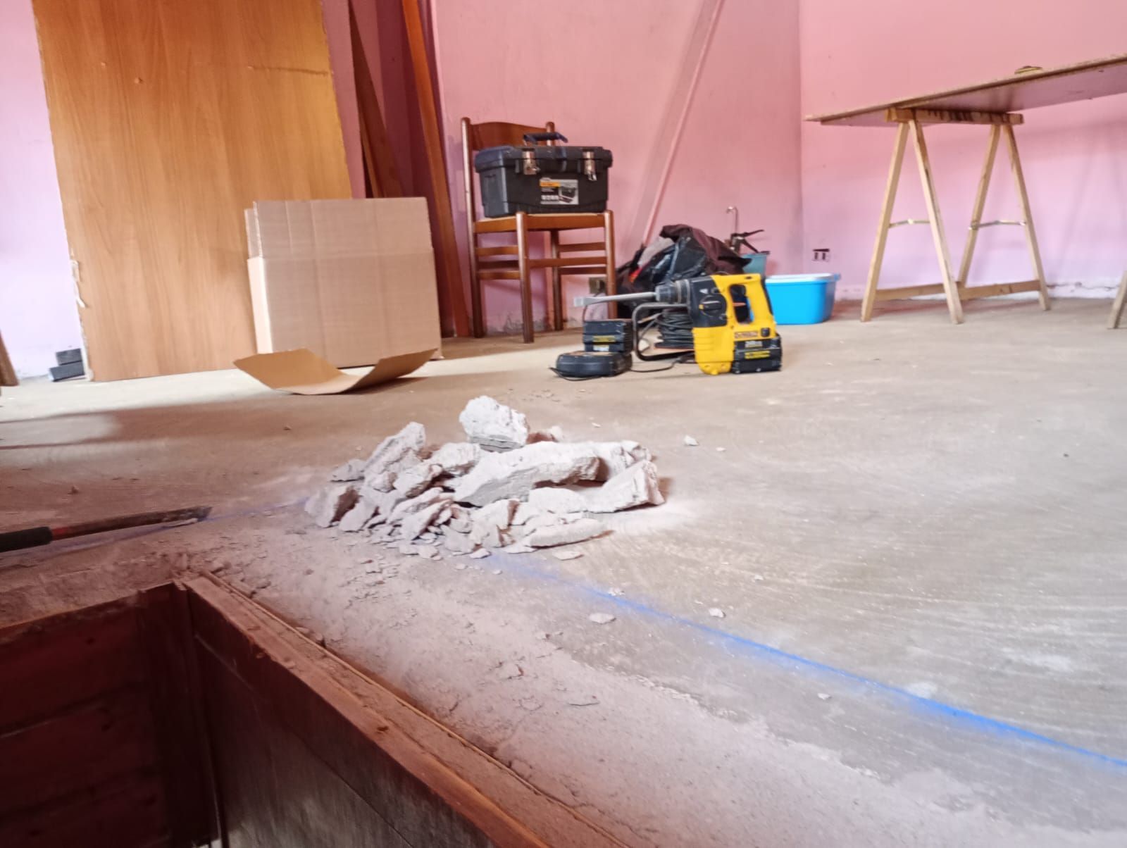 Attrezzi da costruzione e detriti su un pavimento di cemento in una stanza non rifinita con pareti rivestite in legno.
