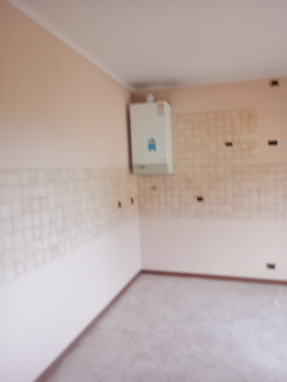 Stanza vuota piastrellata con pareti beige e caldaia a muro in un angolo.