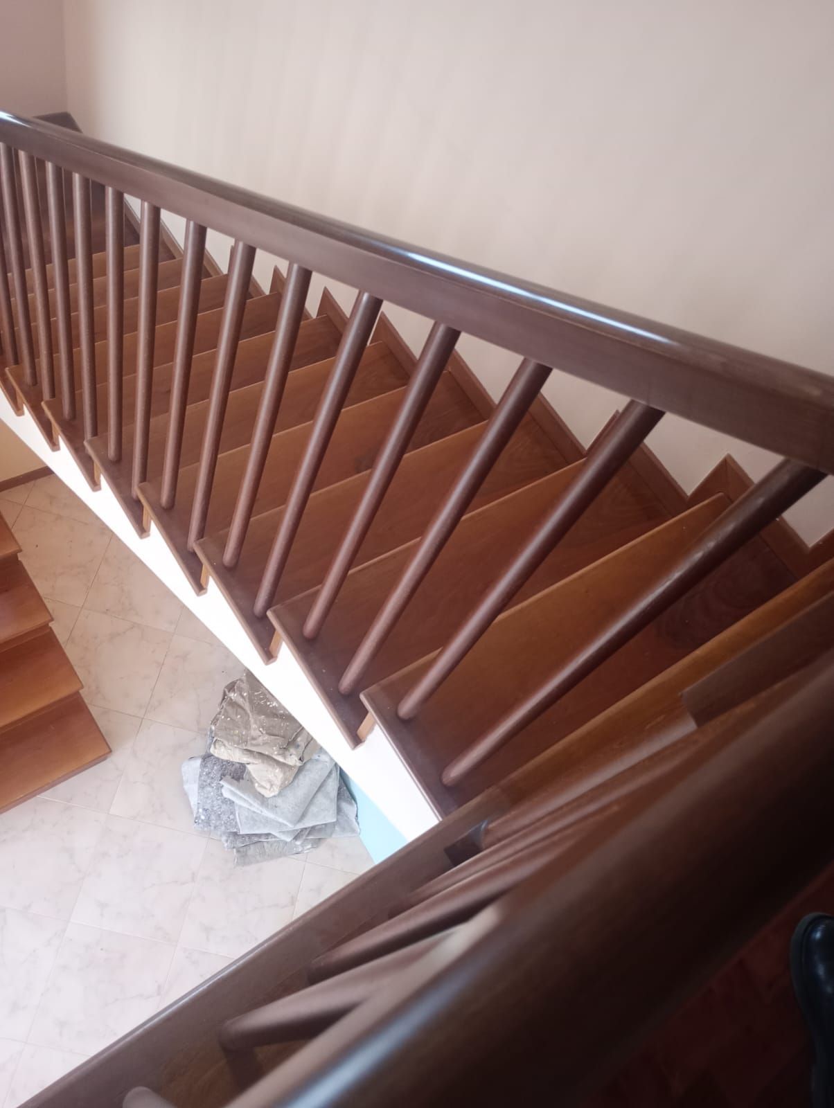 Ringhiera in legno accanto a una luminosa tromba delle scale con pareti color crema e pavimento piastrellato.