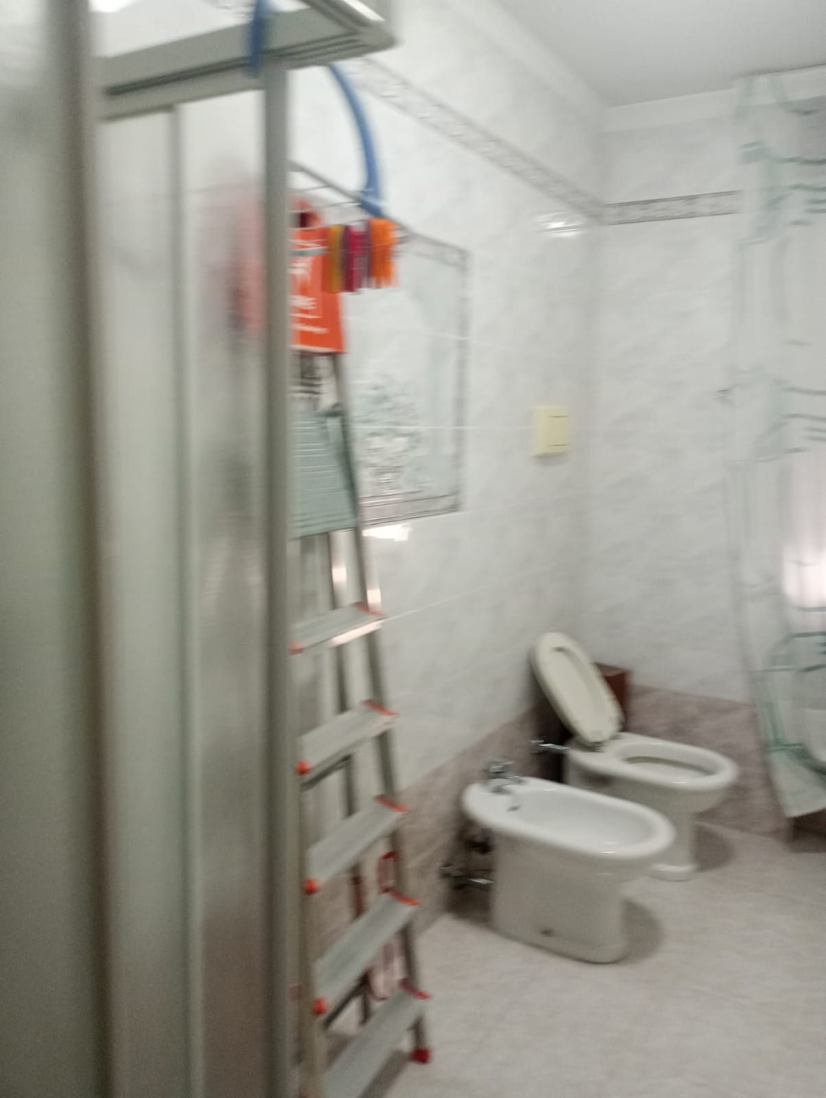 Bagno piccolo con scaletta, accessori arancioni a parete e WC con bidet accanto alla zona doccia.