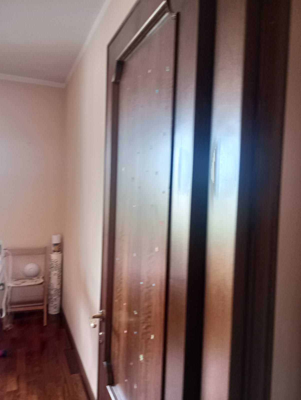 Stretto corridoio con una porta di legno scuro chiusa e una piccola sedia bianca in fondo.