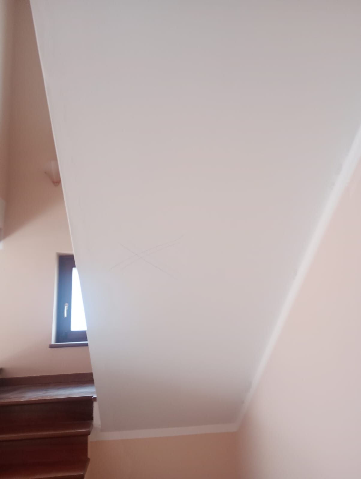 Vano scale con pareti bianche, gradini in legno e una piccola finestra che lascia entrare la luce