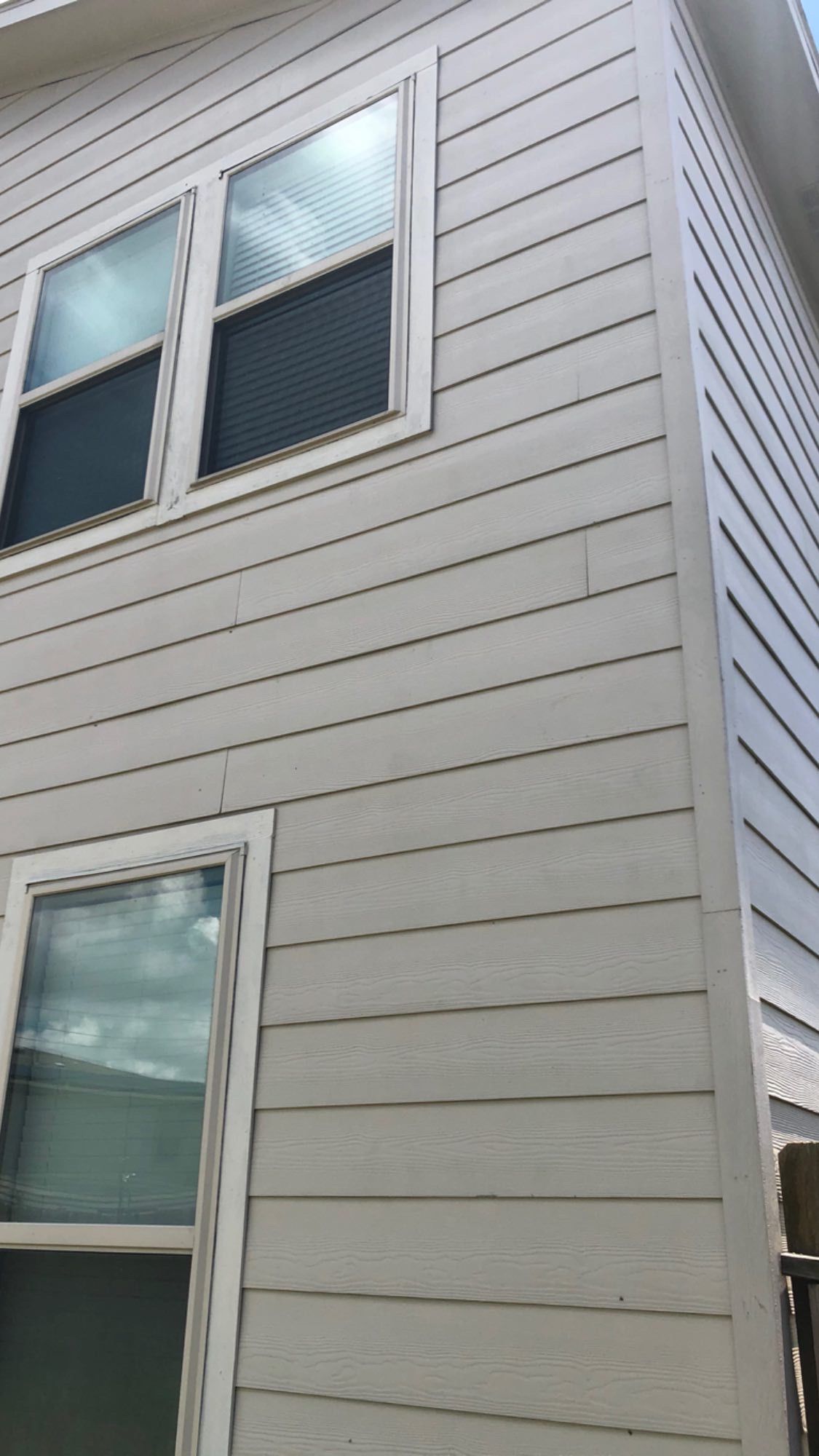White house exterior with light gray siding and two windows on the corner wall.