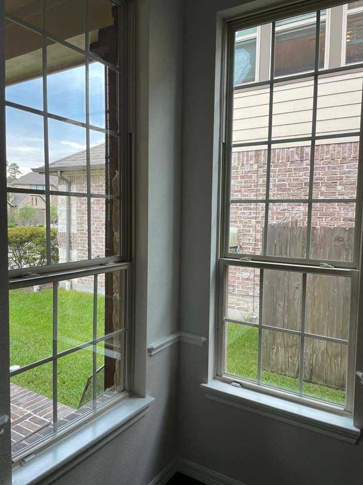 Sunlit corner with two tall windows, green lawn outside, and beige siding on a building beyond.