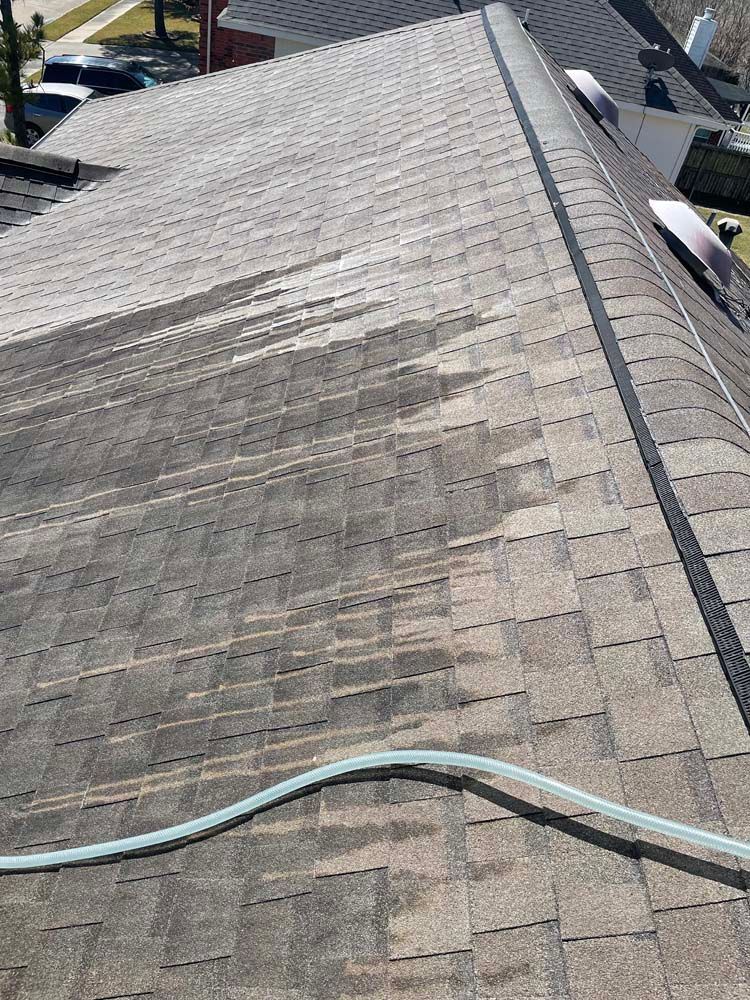 Weathered gray shingle roof with a hose stretched across the foreground, viewed from above.