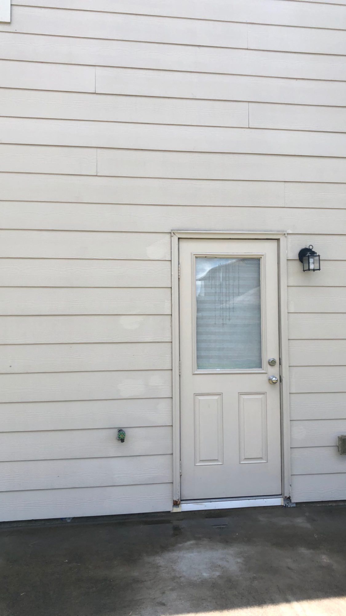 Beige exterior door with window on a light-sided building, beside a wall-mounted light fixture.