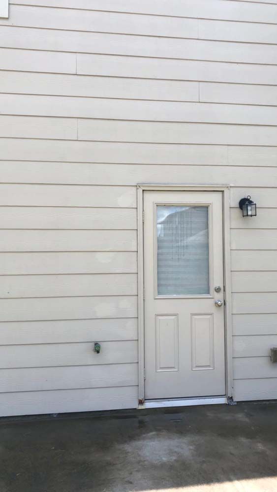 White exterior door with a small window on a beige house wall, beside a wall light.