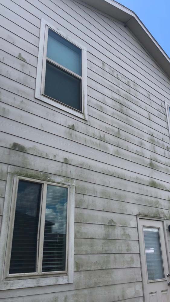 House exterior with gray siding and visible mildew stains around the windows and lower wall.