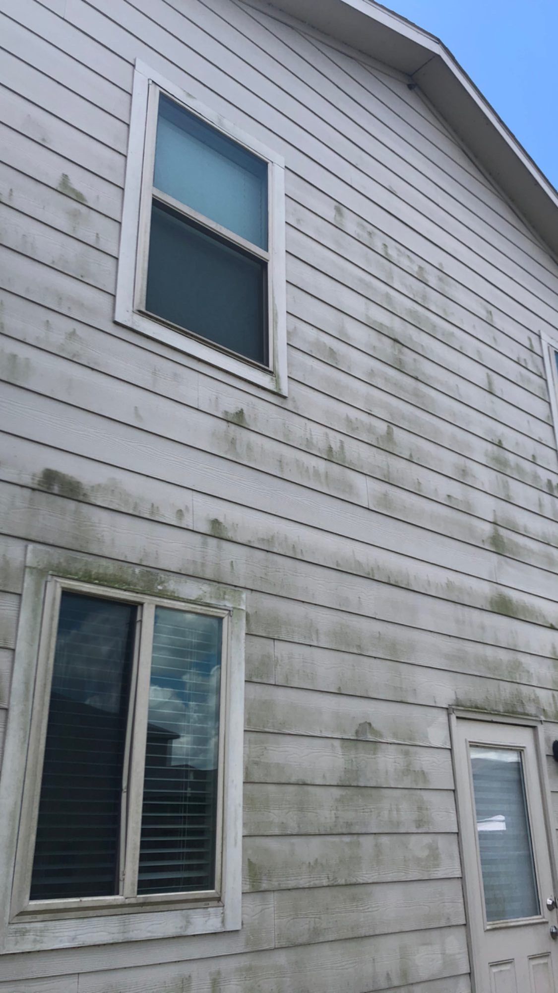 Two-story white house siding with dark streak stains and several windows