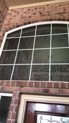 Arched window with white grid panes above a brick-front house entrance