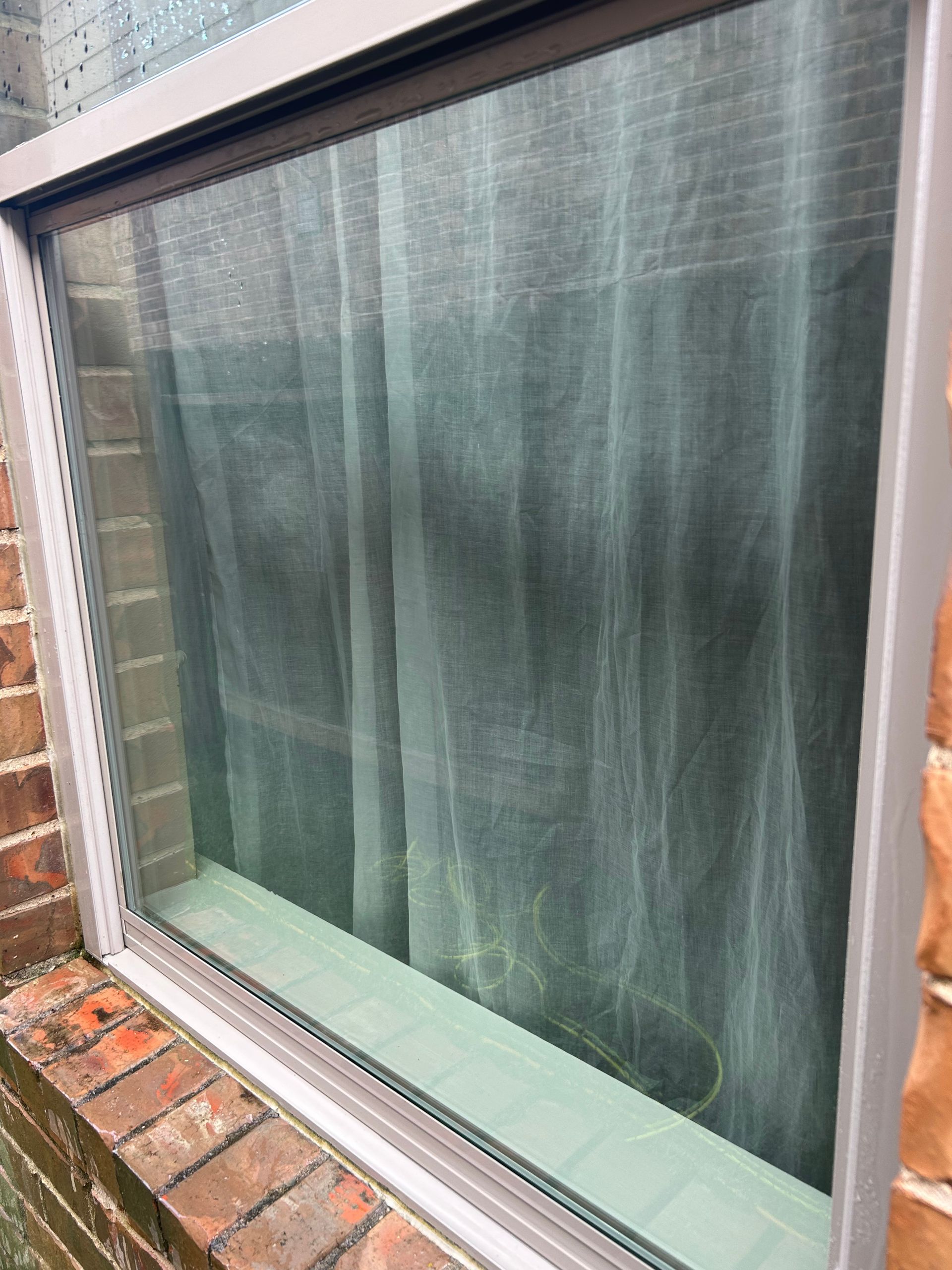 Rain-streaked window with a dark curtain, framed by brick wall and white trim