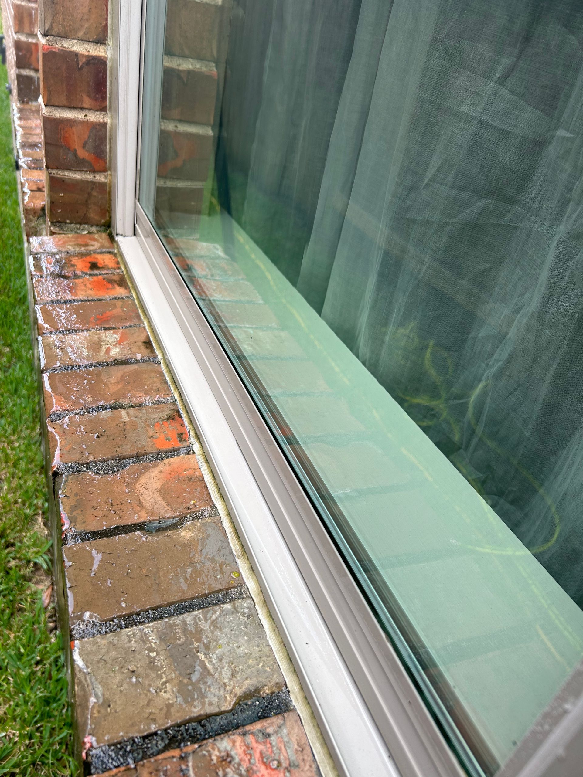 Close-up of a brick windowsill and white window frame beside a green-tinted window pane.
