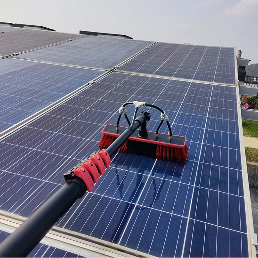 Solar panels being cleaned with a red brush attachment on a roof.