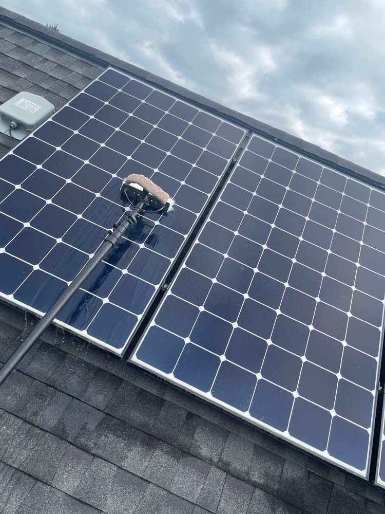 Solar panels on a sloped roof with a person cleaning them under a cloudy sky