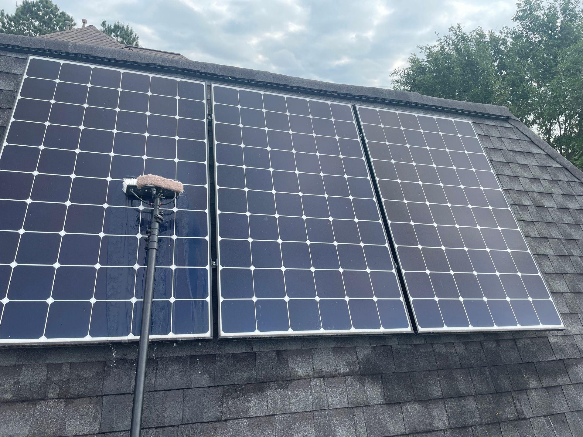 Solar panels mounted on a shingled roof under a cloudy sky, with a small rooftop device in front.