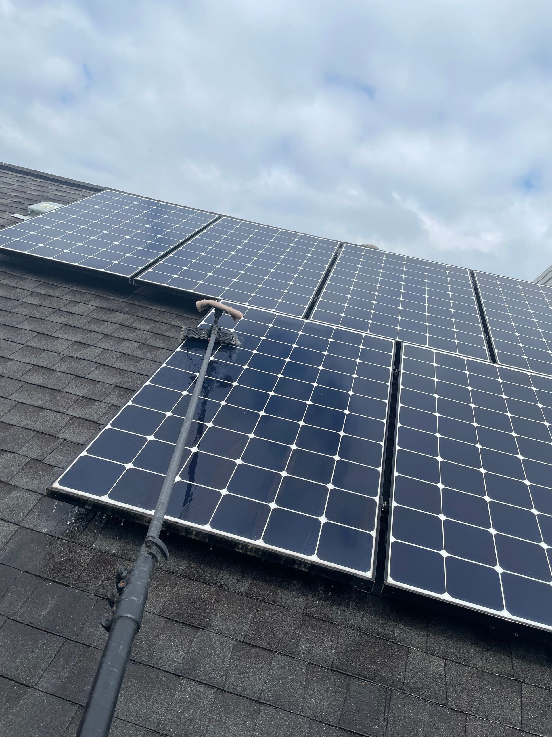 Solar panels installed on a shingled roof under a cloudy sky