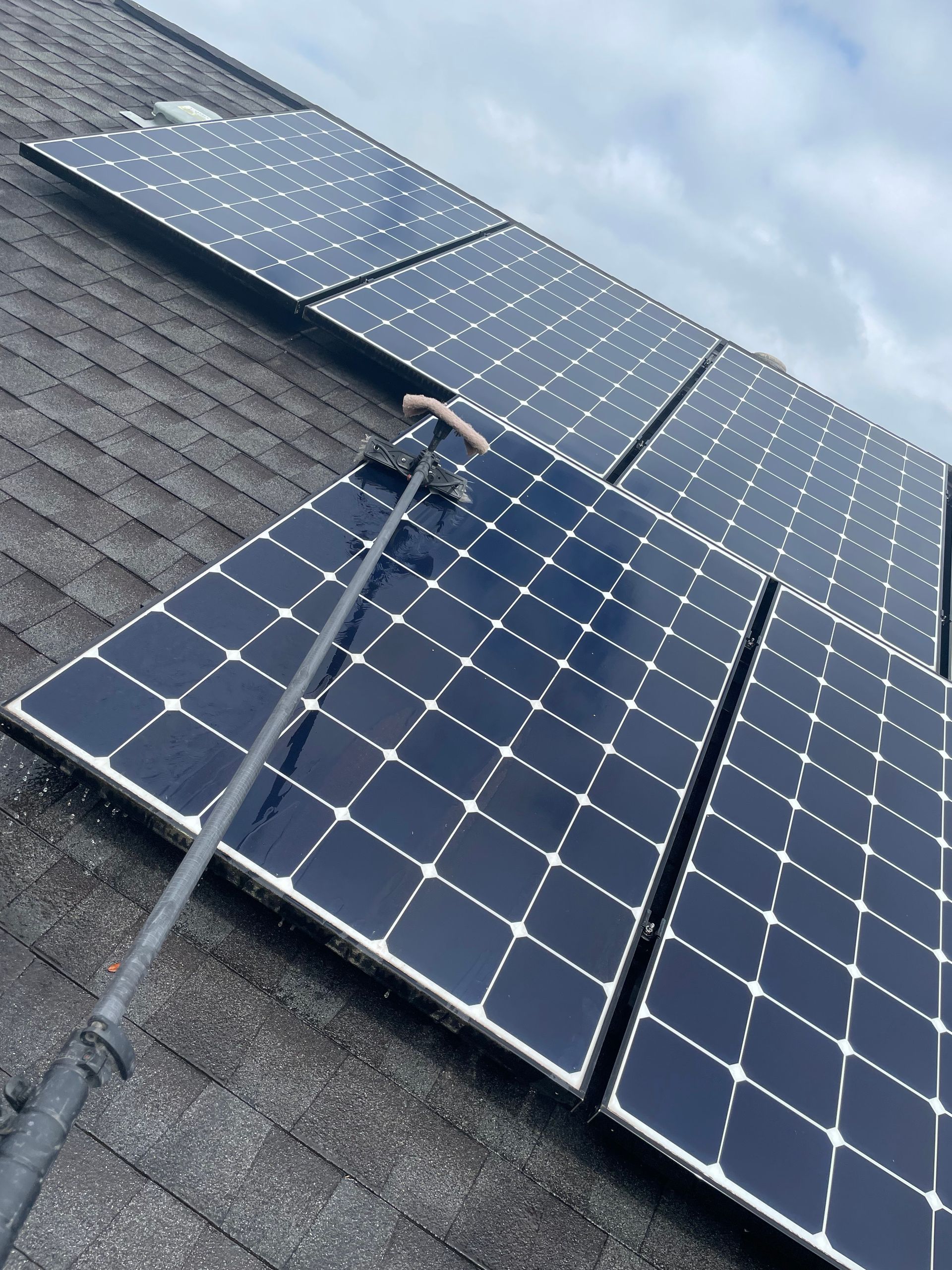 Solar panels mounted on a steep shingled roof under a cloudy sky