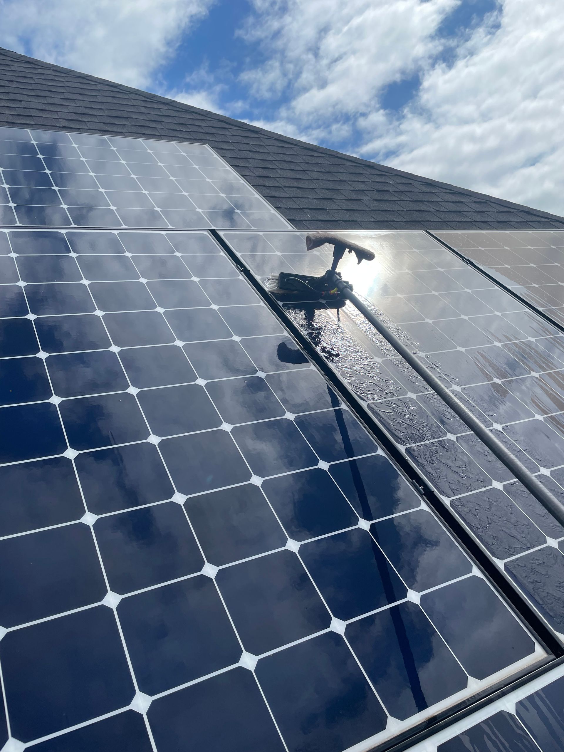 Person pressure-washing solar panels on a roof in sunlight