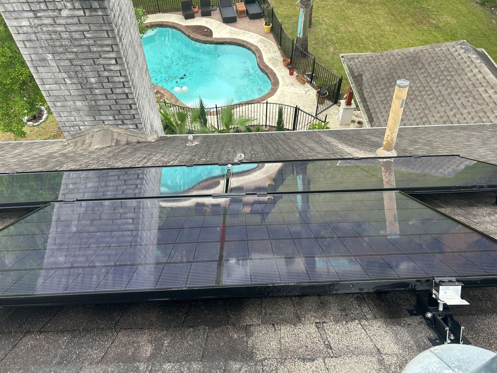 Rooftop view of a swimming pool, seen beyond a glass railing and rooftop shingles