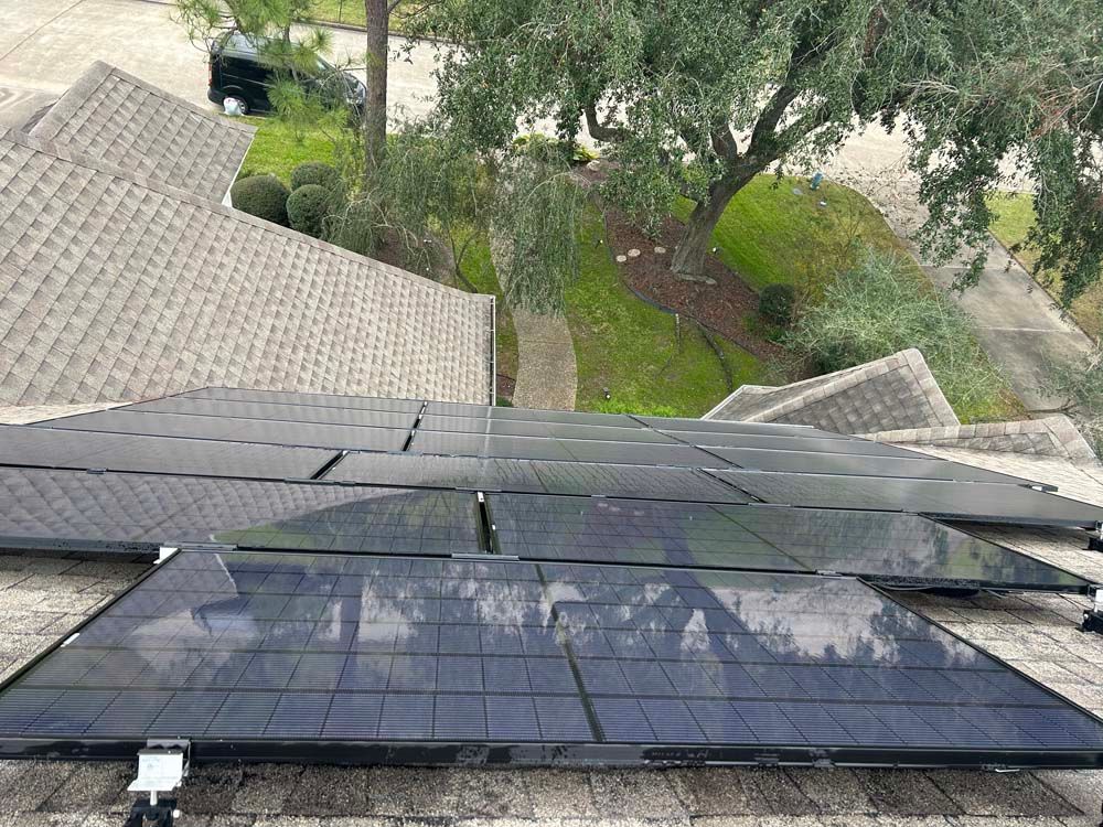 Solar panels mounted on a rooftop, overlooking trees and a driveway below.