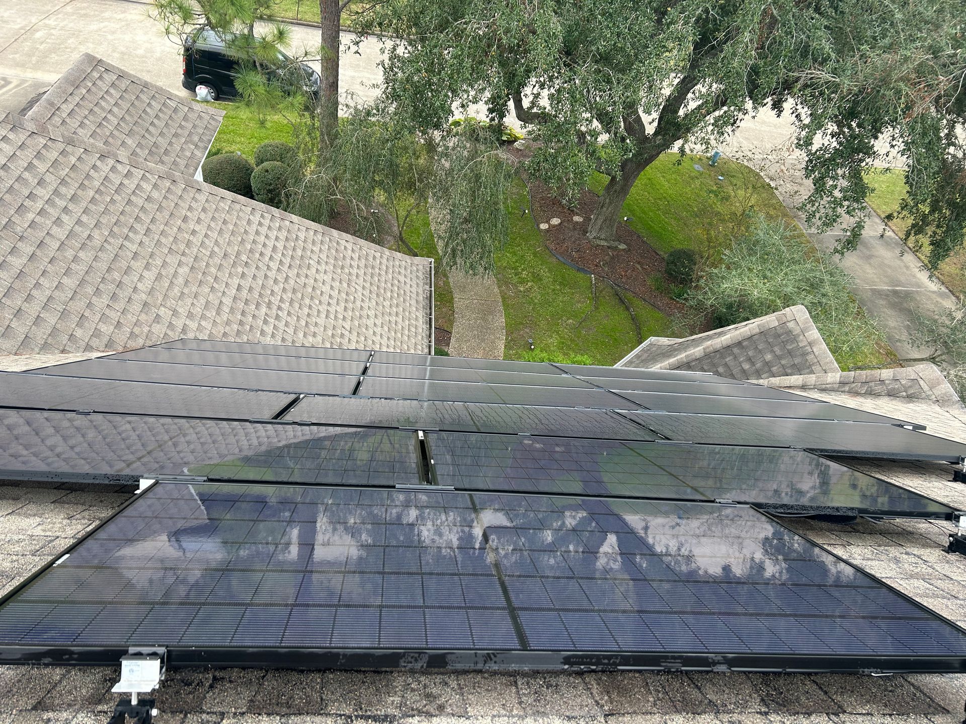 Solar panels mounted on a roof, overlooking trees and a yard below.